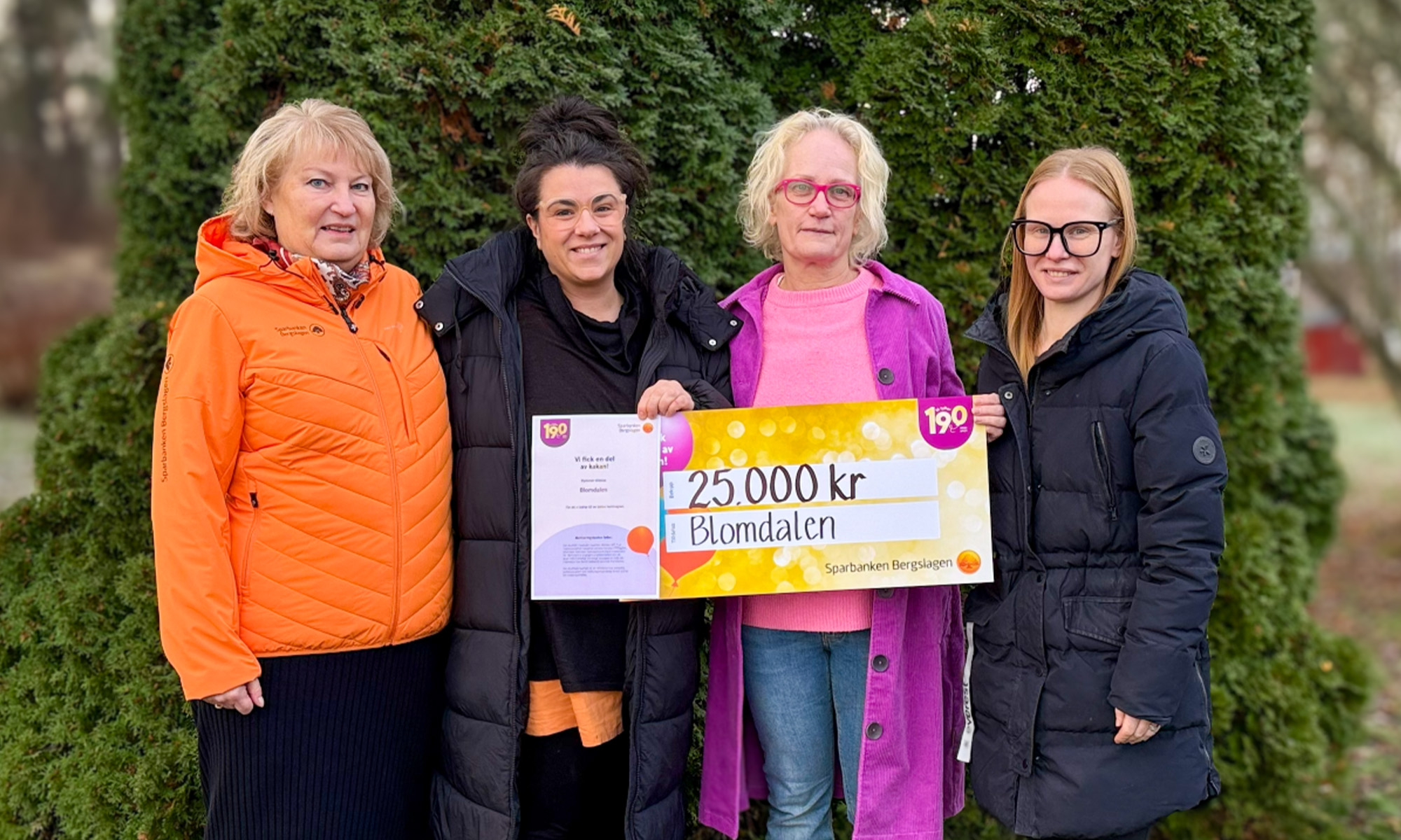 Bild på personal från banken samt tre vinnare som håller i värdebevis, utomhus