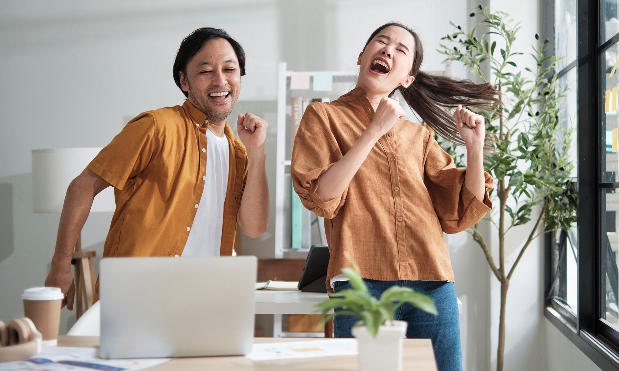 En glad man och kvinna dansar framför ett skrivbord med en laptop på