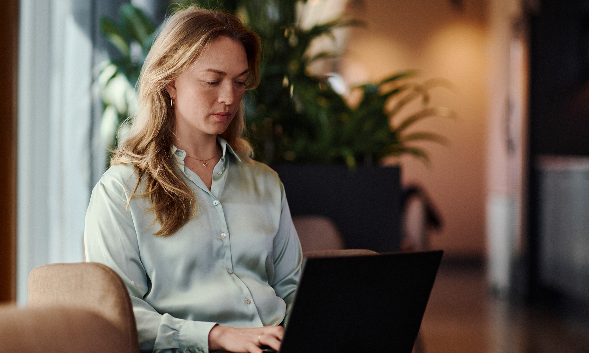 Kvinna som sitter med sin laptop i knät och skriver