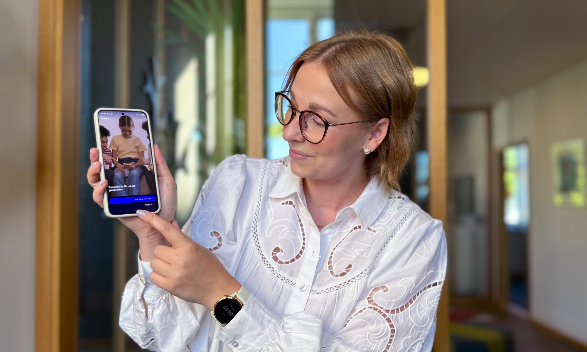 En kvinna håller upp en telefon och pekar på skärmen som visar Gimi-appen.