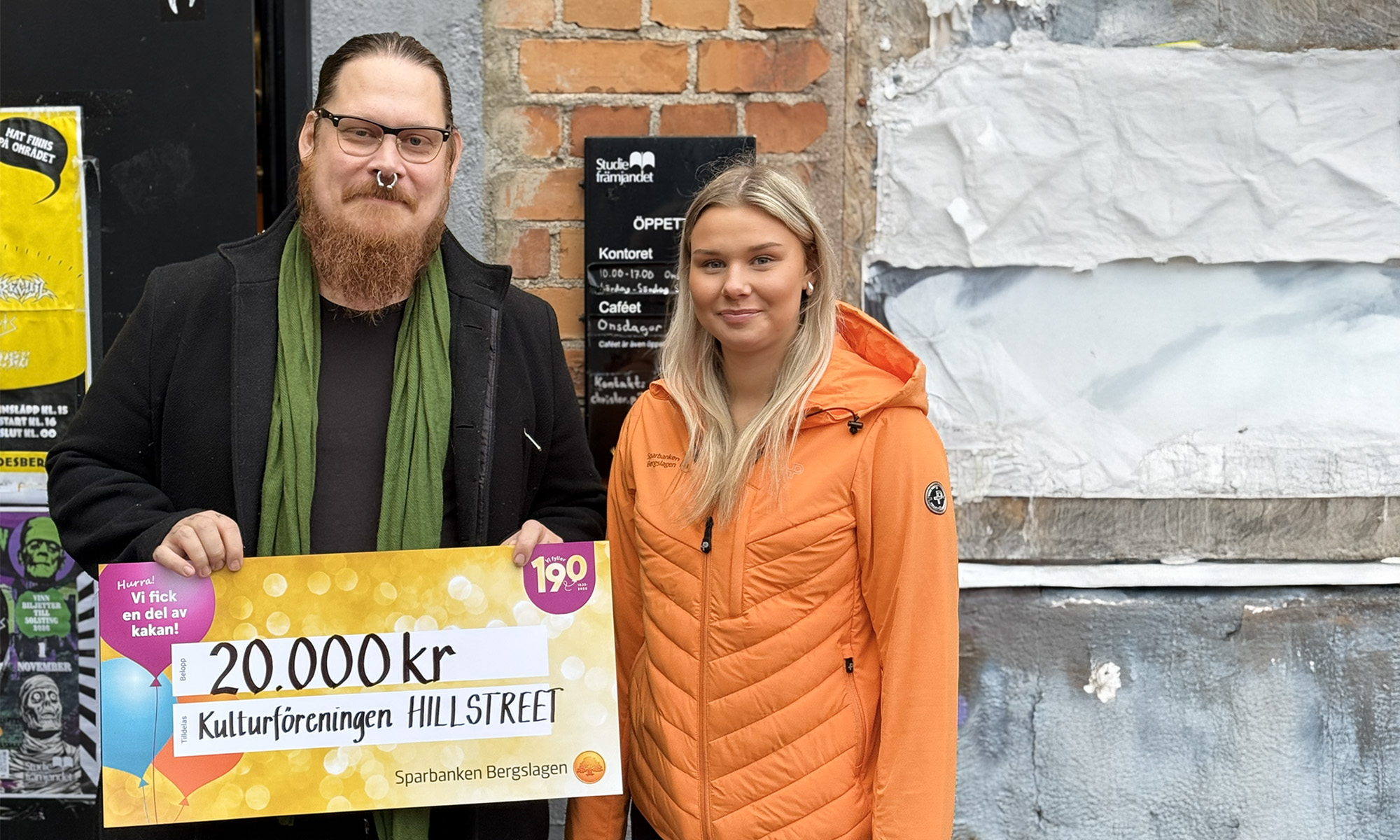 En man från Hillstreet och kvinna från banken står och visar upp vinstchecken på 20 000kr..