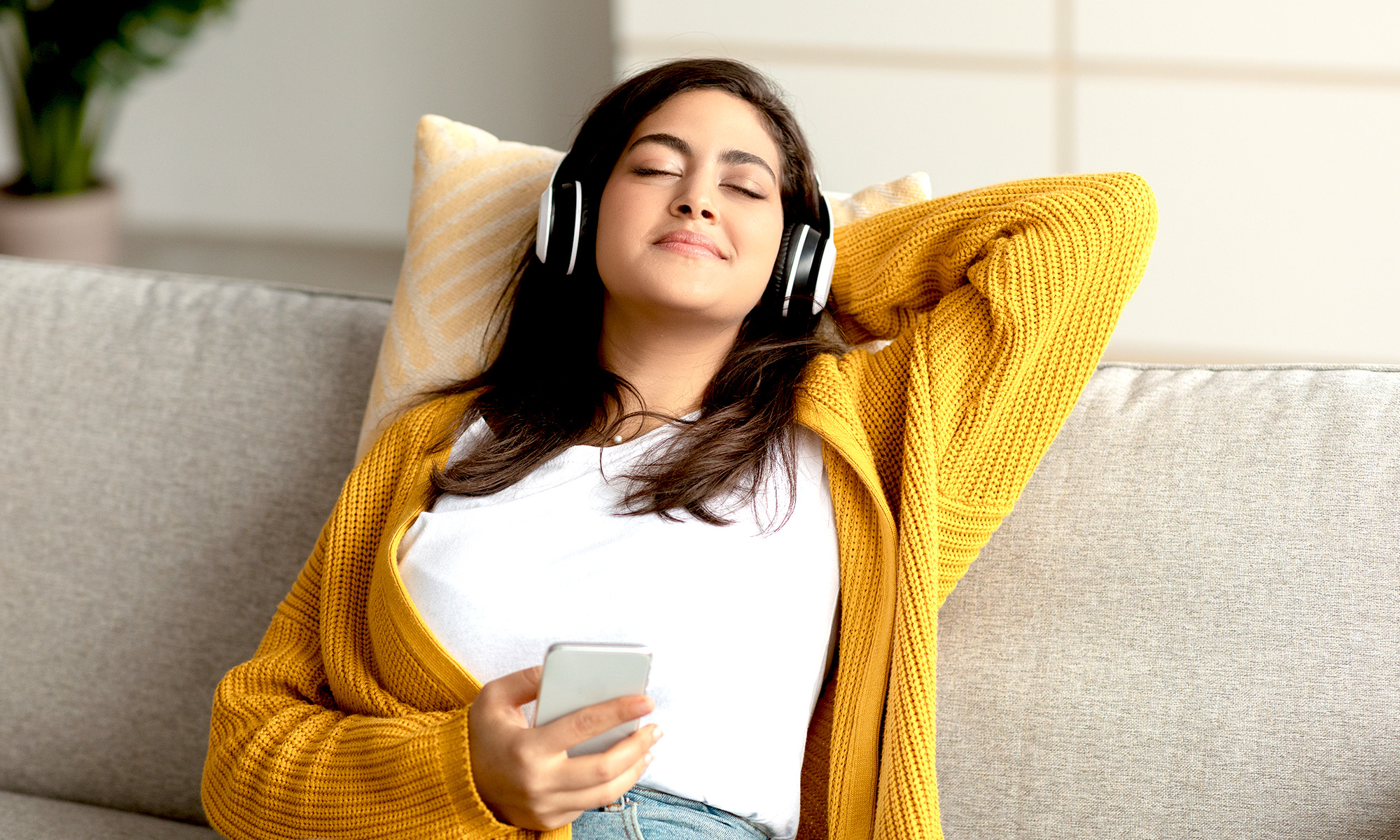 En ung tjej med hörlurar sitter tillbakalutad i en soffa med slutna ögon